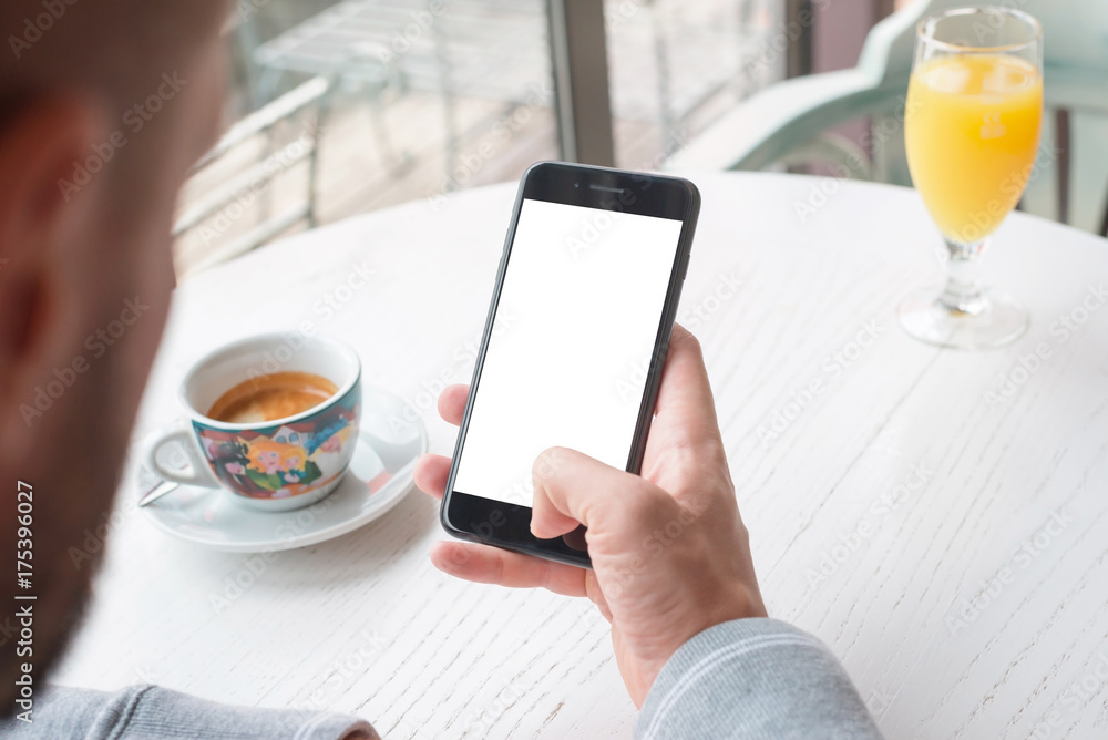 Poster Phone mockup for user interface design promotion. Man hold smart phone in right hand. Coffee and juice on white wooden desk in background.