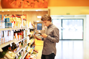 Man shopping in supermarket reading product information