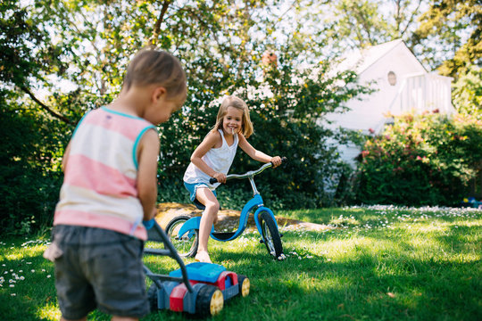 Little girl and boy playing together in backyard with bike and lawmower