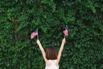 Young girl standing backwards against a wall of ivy holding small American flags