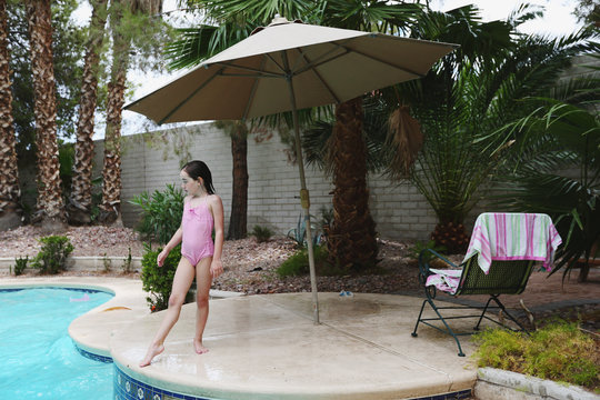 Girl in pink swimming suit stands at edge of pool