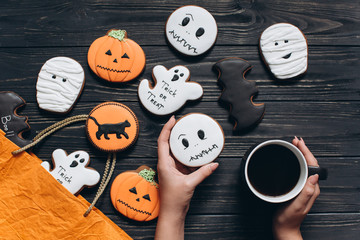 Girl holding cup of coffee and gingerbread for Halloween on a black wooden background.