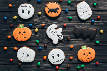 A colors candy and scary gingerbreads for Halloween on a black wooden background.