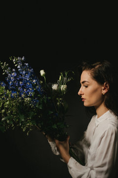 Model with white button up shirt, purple flower bouquet in basement lit by natural window light