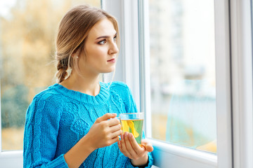 Young beautiful woman looking out the window and drinking tea. The concept of lifestyle, autumn and comfort.