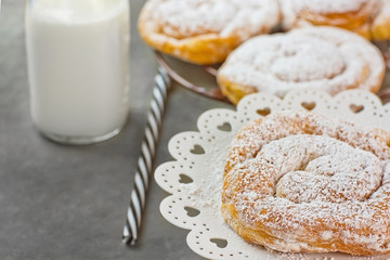 Swirl Danish Pastry Powdered on Cooling Rack and Cake Stand. Bottle of Milk Striped Straw. Dark Tabletop.