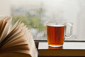 a cup of tea on the window and an open book, autumn rain outside the window, a concept of relaxation