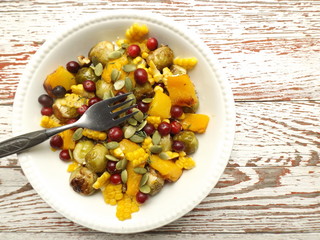 Warm salad of baked pumpkin and Brussels sprouts with corn and cranberries. Vegetarian healthy food.