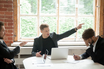 Strict boss, telling upset male employee to leave meeting room during briefing, pointing his finger to the way out. Executive team member scolding colleague, CEO dismissing coworker in front of team.