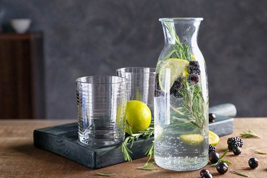 Bottle with fresh rosemary drink and empty glasses on table
