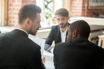 Rear view of serious boss holding financial stats report and scolding african-american employee...