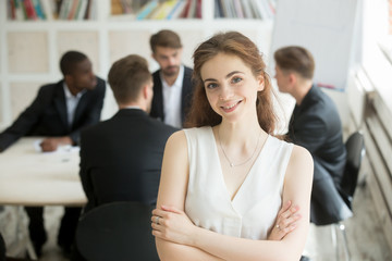 Obraz premium Headshot of attractive young smiling businesswoman looking at camera. Blurry team of male businessmen on background, Friendly female executive, company representative, corporate worker or manager .