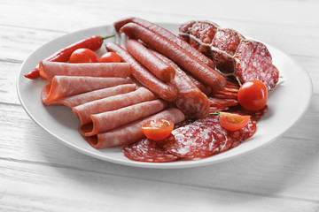 Plate with delicious sliced sausages on wooden table