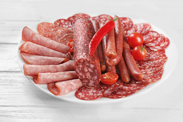 Plate with delicious sliced sausages on wooden table