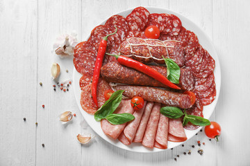 Plate with delicious sliced sausages on wooden table