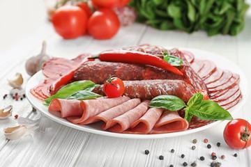 Plate with delicious sliced sausages on wooden table