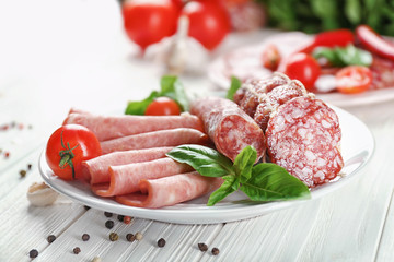Plate with delicious sliced sausages on wooden table