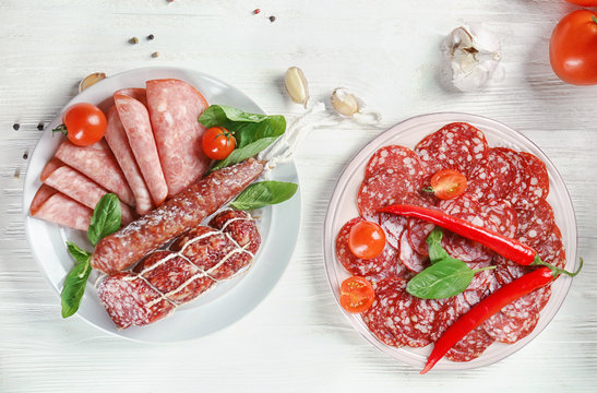 Plates with delicious sliced sausages on wooden table