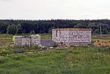 Стройплощадка с недостроенным домом из белого кирпича на поле в траве