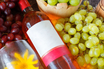 Bunches of fresh different ripe grapes and a bottle of rose wine on  wooden textural surface. space...