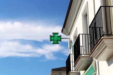 Pharmazie, grünes Kreuz, Symbol, Gebäude auf der rechten Seite, blauer Himmel links, Spanien