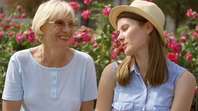 Family enjoying summer trip to Paris. Mother and young daughter having great time sitting on bench on street near beautiful pink frowers relaxing, chatting. Happy family enjoying vacation together
