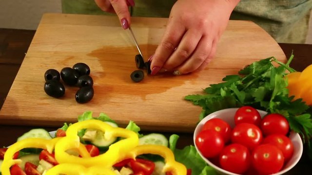 A woman knives the regimen into small pieces of black olives. Close-up. Shot with dolly from from left to left
