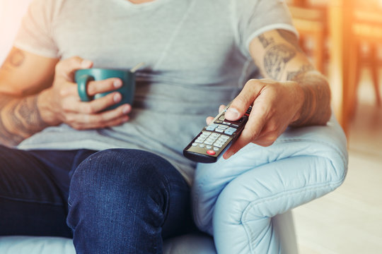 man drinking tea and  watching tv with remote control