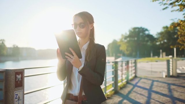 Young Businesswoman Using Digital Tablet, Going to Work in the Sunny Morning City. SLOW MOTION. STEADICAM Stabilized Shot. Attractive Professional Business Woman walking to job. Lens Flare. 