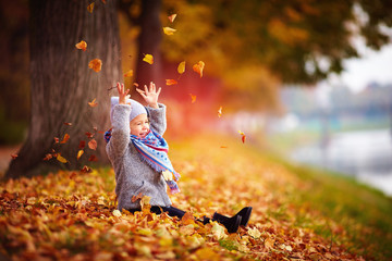 adorable happy baby girl catching the fallen leaves, playing in the autumn park