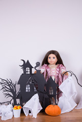 A decorative haunted house with ghosts and a pumpkin in front. A doll in a Halloween costume is decoration the house. 