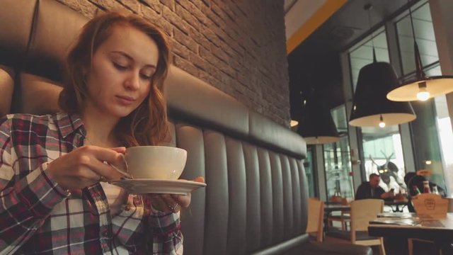Woman drinking coffee in a cafe, 4K Slow Motion 120 fps. Stabilazed dolly shot. Young beautiful calm woman enjoying a cup of hot coffee in the restaurant. Relaxed morning breakfast in a city. 
