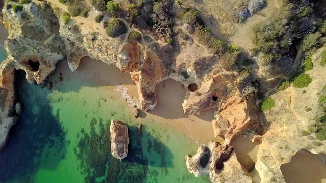 Aerial shot from above of blue water of ocean washing calmly white rocky cliffs and sand of tropical shoreline in Portugal, Algarve.