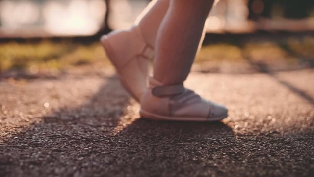 Little baby learns to walk. First Steps. Slow Motion 120 fps, 4K. Mother is teaching her child to do the first steps on a park road in summer. Close up on feet. Happy childhood and Maternity. Family