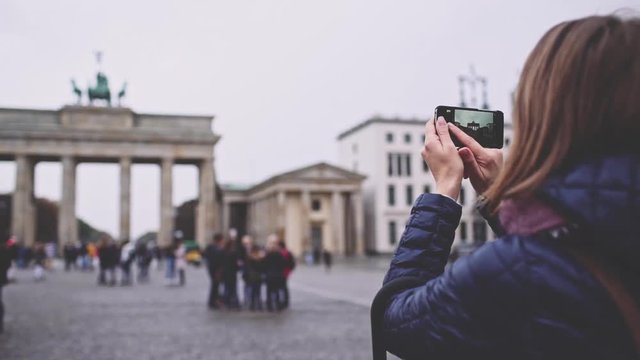 Woman Taking Pictures of Brandenburg Gate in Berlin with SmartPhone. SLOW MOTION. Young woman tourist with cellphone photographing Brandenburger Tor. Travel in Germany.