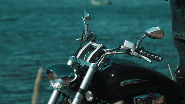 Black chopper bike standing on blue sea shore on summer sunny windy day, close up shot