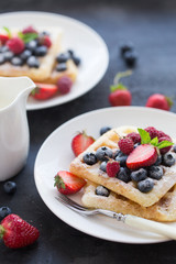 Belgian waffles with fresh berries on white plate.