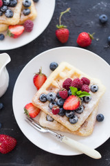 Belgian waffles with fresh berries on white plate.