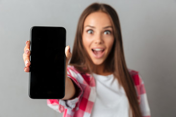 Amazed pretty young woman showing blank screen phone, selective focus