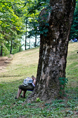 old woman reads magazine under a tree