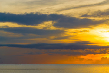 The sun shines through the clouds at dawn on the shore of the Gulf of Thailand.