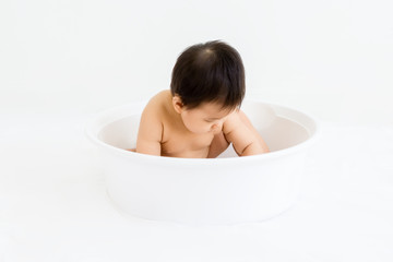 Portrait of adorable baby sitting in the basin for shower, indoors