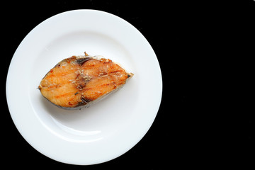 A grilled mackerel fish on white plate  over black background