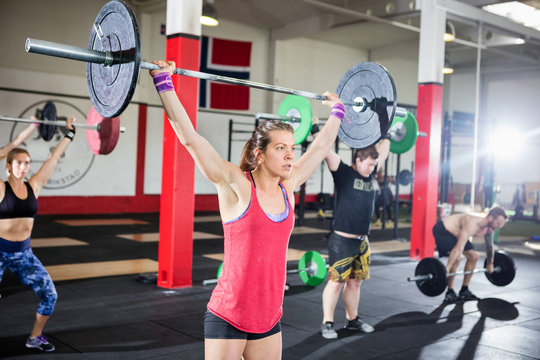 Woman Lifting Barbell With Friends In Fitness Studio