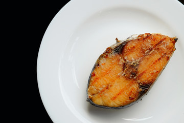 A grilled mackerel fish on white plate  over black background