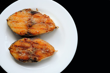 A grilled mackerel fish on white plate  over black background