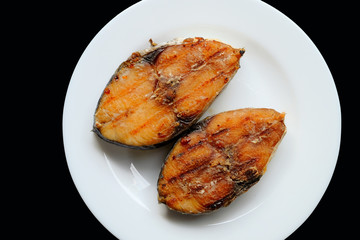 A grilled mackerel fish on white plate  over black background