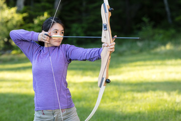 Female Athlete Aiming With Bow And Arrow In Forest