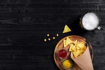 Top view of tortilla chips with sauce, glass of beer on black wooden background