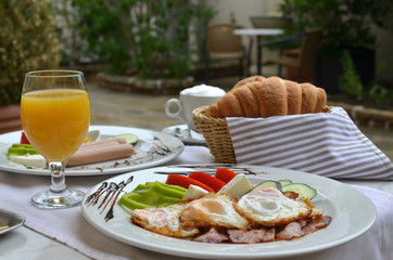 Plate with rich and colorful American breakfast - fried eggs, bacon, sausages, croissants and juice